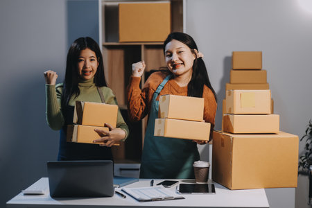 Startup SME small business entrepreneur of freelance Asian woman wearing apron using laptop and box to receive and review orders online to prepare to pack sell to customers, online sme business ideas.の写真素材