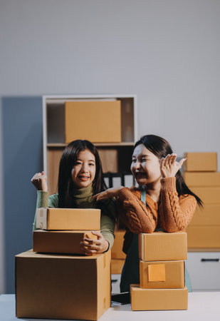 Startup SME small business entrepreneur of freelance Asian woman wearing apron using laptop and box to receive and review orders online to prepare to pack sell to customers, online sme business ideas.の写真素材