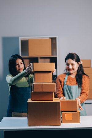 Startup SME small business entrepreneur of freelance Asian woman wearing apron using laptop and box to receive and review orders online to prepare to pack sell to customers, online sme business ideas.の写真素材