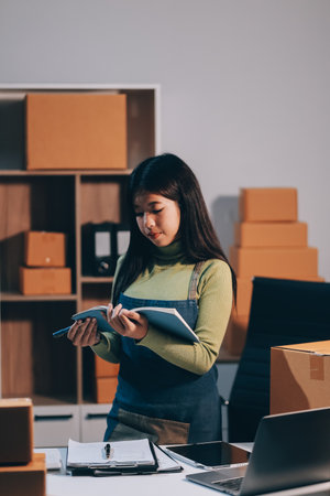 Startup SME small business entrepreneur of freelance Asian woman wearing apron using laptop and box...