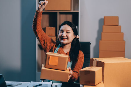 Startup SME small business entrepreneur of freelance Asian woman wearing apron using laptop and box to receive and review orders online to prepare to pack sell to customers, online sme business ideas.の写真素材