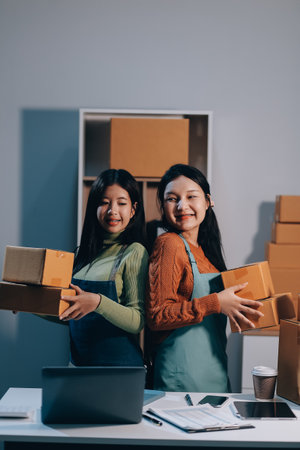 Startup SME small business entrepreneur of freelance Asian woman wearing apron using laptop and box to receive and review orders online to prepare to pack sell to customers, online sme business ideas.の写真素材