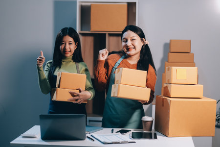Startup SME small business entrepreneur of freelance Asian woman wearing apron using laptop and box to receive and review orders online to prepare to pack sell to customers, online sme business ideas.の写真素材