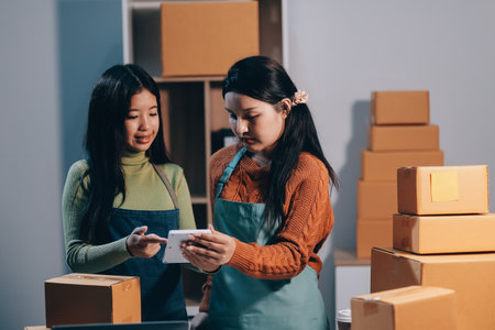 Startup SME small business entrepreneur of freelance Asian woman wearing apron using laptop and box to receive and review orders online to prepare to pack sell to customers, online sme business ideas.の写真素材