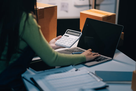 Startup SME small business entrepreneur of freelance Asian woman wearing apron using laptop and box to receive and review orders online to prepare to pack sell to customers, online sme business ideas.の写真素材