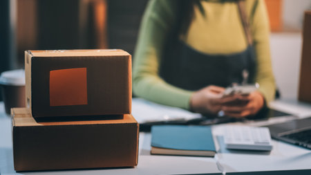 Startup SME small business entrepreneur of freelance Asian woman wearing apron using laptop and box to receive and review orders online to prepare to pack sell to customers, online sme business ideas.の写真素材