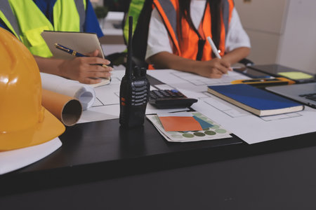 Closeup of team of industrial engineers meeting analyze machinery blueprints consult project on table in manufacturing factory. Working in manufacturing plant or production plant.の写真素材