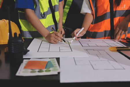 Closeup of team of industrial engineers meeting analyze machinery blueprints consult project on table in manufacturing factory. Working in manufacturing plant or production plant.の写真素材