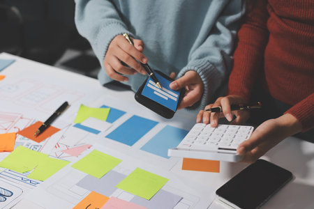 UX UI designer testing prototype on a phone, discussing and brainstorming on wireframes for a website and mobile app prototype, in the concept of website and mobile application design concept.の写真素材