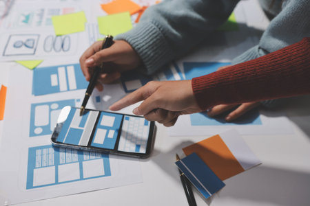 UX UI designer testing prototype on a phone, discussing and brainstorming on wireframes for a website and mobile app prototype, in the concept of website and mobile application design concept.の写真素材