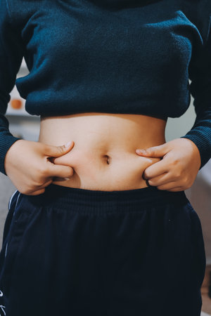 woman's hand holding excessive belly fat, overweight concept