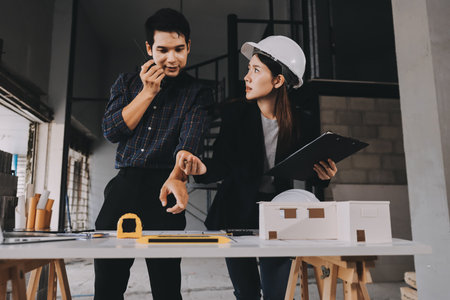 Construction manager and engineer dressed in orange work vests and hard helmets explore construction documentation on the building site near the steel framesの写真素材