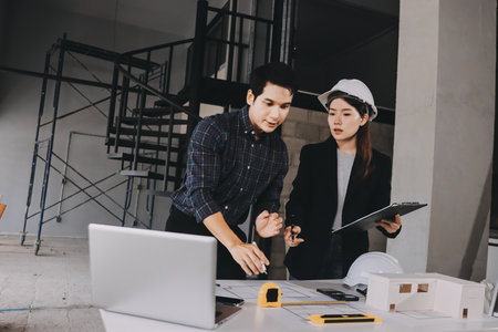 Construction manager and engineer dressed in orange work vests and hard helmets explore construction documentation on the building site near the steel framesの写真素材