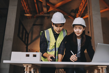 Construction manager and engineer dressed in orange work vests and hard helmets explore construction...
