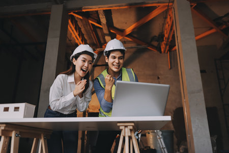 Construction manager and engineer dressed in orange work vests and hard helmets explore construction...