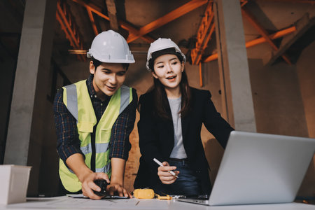 Construction manager and engineer dressed in orange work vests and hard helmets explore construction...