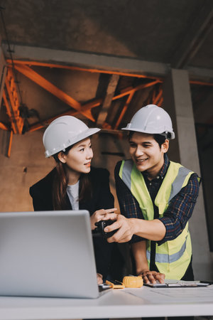 Construction manager and engineer dressed in orange work vests and hard helmets explore construction...