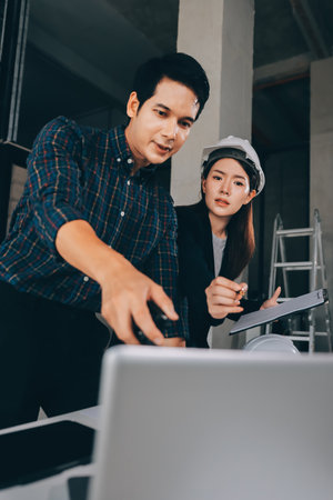Construction manager and engineer dressed in orange work vests and hard helmets explore construction documentation on the building site near the steel framesの写真素材