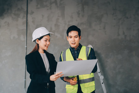 Construction manager and engineer dressed in orange work vests and hard helmets explore construction...