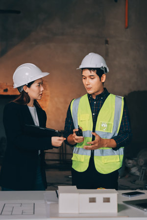 Construction manager and engineer dressed in orange work vests and hard helmets explore construction...