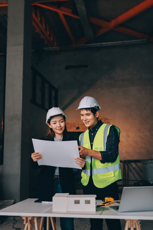 Construction manager and engineer dressed in orange work vests and hard helmets explore construction documentation on the building site near the steel framesの写真素材