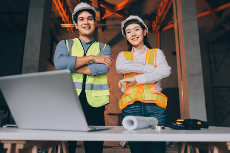Construction manager and engineer dressed in orange work vests and hard helmets explore construction documentation on the building site near the steel framesの写真素材