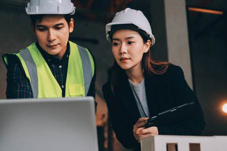Construction manager and engineer dressed in orange work vests and hard helmets explore construction documentation on the building site near the steel framesの写真素材