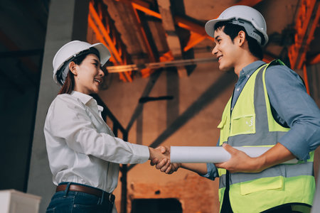 Construction manager and engineer dressed in orange work vests and hard helmets explore construction...