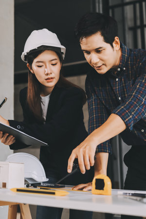 Construction manager and engineer dressed in orange work vests and hard helmets explore construction documentation on the building site near the steel framesの写真素材