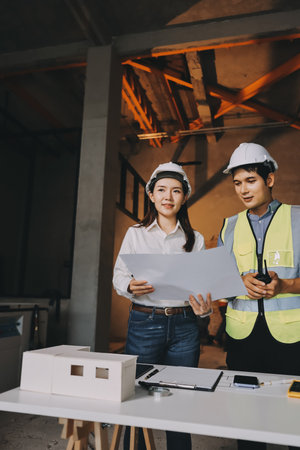 Construction manager and engineer dressed in orange work vests and hard helmets explore construction...