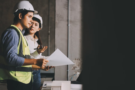 Construction manager and engineer dressed in orange work vests and hard helmets explore construction...