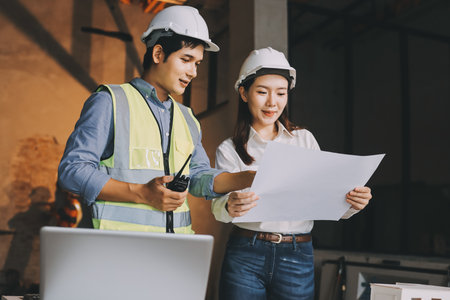 Construction manager and engineer dressed in orange work vests and hard helmets explore construction documentation on the building site near the steel framesの写真素材