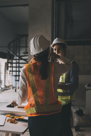 Construction manager and engineer dressed in orange work vests and hard helmets explore construction documentation on the building site near the steel framesの写真素材