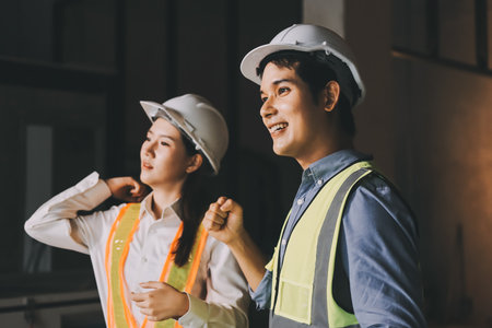 Construction manager and engineer dressed in orange work vests and hard helmets explore construction...