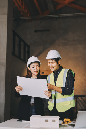 Construction manager and engineer dressed in orange work vests and hard helmets explore construction documentation on the building site near the steel framesの写真素材