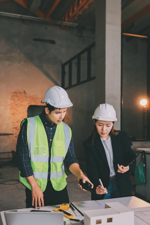 Construction manager and engineer dressed in orange work vests and hard helmets explore construction...