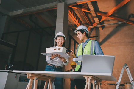 Construction manager and engineer dressed in orange work vests and hard helmets explore construction...
