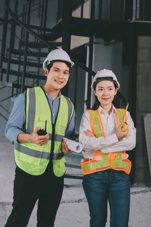 Construction manager and engineer dressed in orange work vests and hard helmets explore construction documentation on the building site near the steel framesの写真素材
