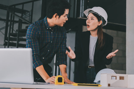 Construction manager and engineer dressed in orange work vests and hard helmets explore construction documentation on the building site near the steel framesの写真素材