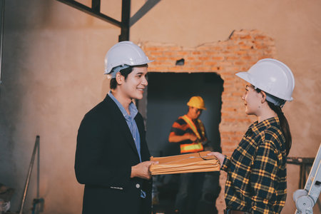 Construction manager and engineer dressed in orange work vests and hard helmets explore construction documentation on the building site near the steel framesの写真素材