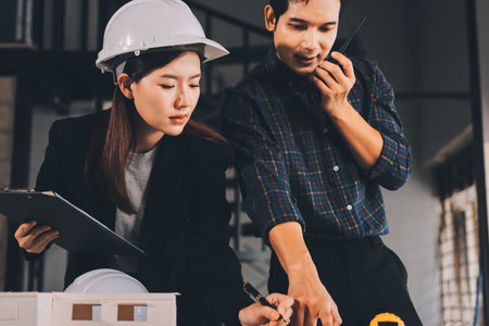 Construction manager and engineer dressed in orange work vests and hard helmets explore construction documentation on the building site near the steel framesの写真素材