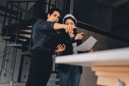 Construction manager and engineer dressed in orange work vests and hard helmets explore construction documentation on the building site near the steel framesの写真素材