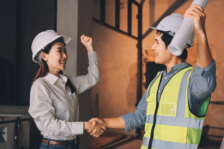 Construction manager and engineer dressed in orange work vests and hard helmets explore construction...