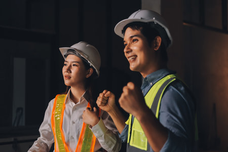 Construction manager and engineer dressed in orange work vests and hard helmets explore construction...