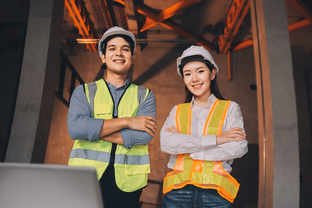 Construction manager and engineer dressed in orange work vests and hard helmets explore construction documentation on the building site near the steel framesの写真素材