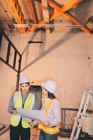 Construction manager and engineer dressed in orange work vests and hard helmets explore construction...
