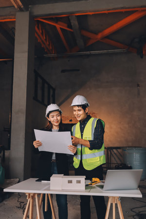 Construction manager and engineer dressed in orange work vests and hard helmets explore construction...