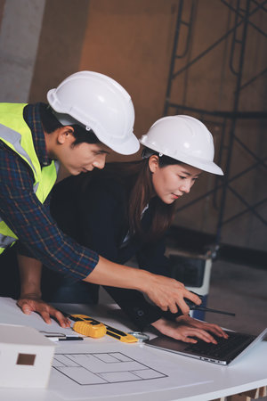 Construction manager and engineer dressed in orange work vests and hard helmets explore construction...