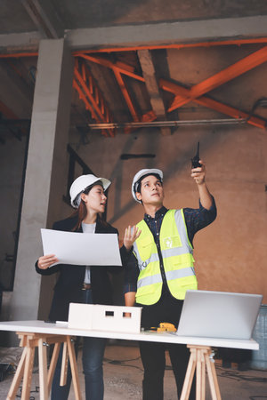 Construction manager and engineer dressed in orange work vests and hard helmets explore construction...