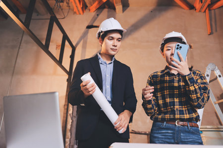 Construction manager and engineer dressed in orange work vests and hard helmets explore construction...
